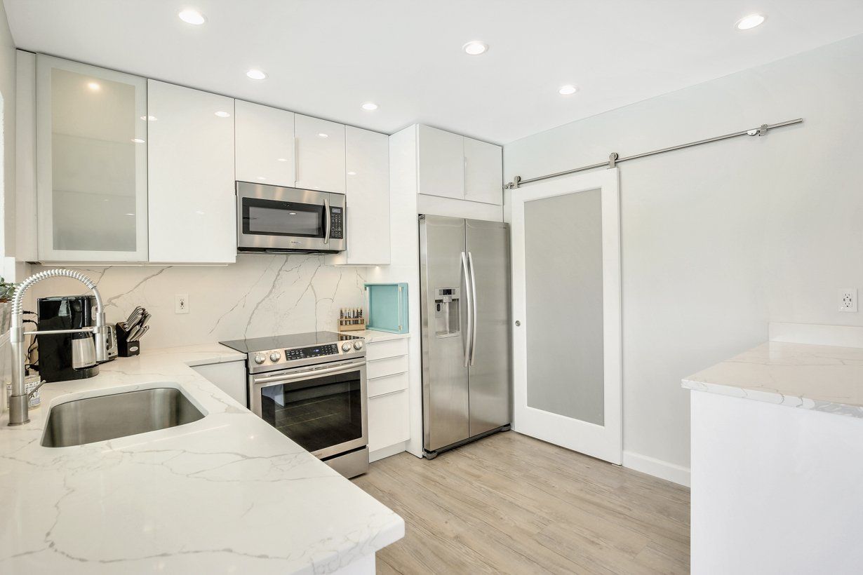 A kitchen with white cabinets , stainless steel appliances , a sink , and a refrigerator.