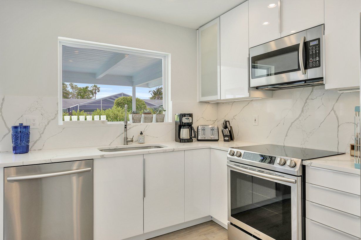 A kitchen with white cabinets , stainless steel appliances , and a large window.