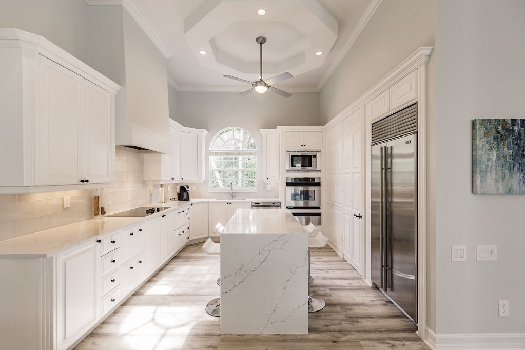 A kitchen with white cabinets , stainless steel appliances , a large island and a ceiling fan.