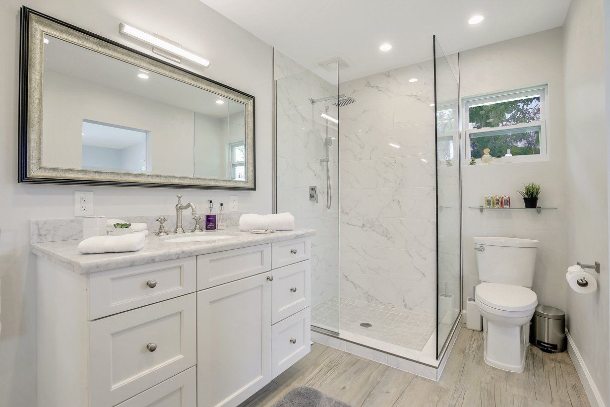 A bathroom with a toilet , sink , mirror and walk in shower.