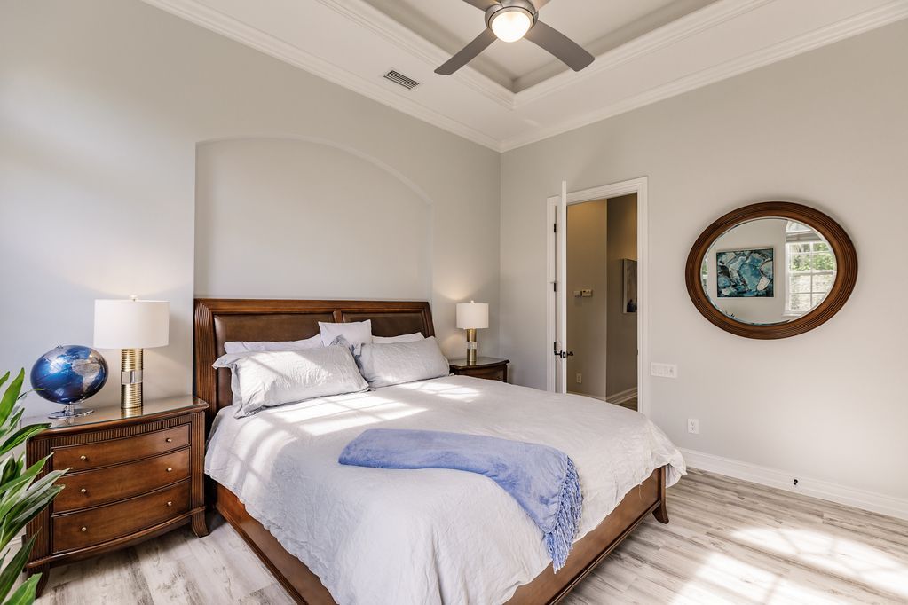 A bedroom with a bed , nightstand , dresser , mirror and ceiling fan.