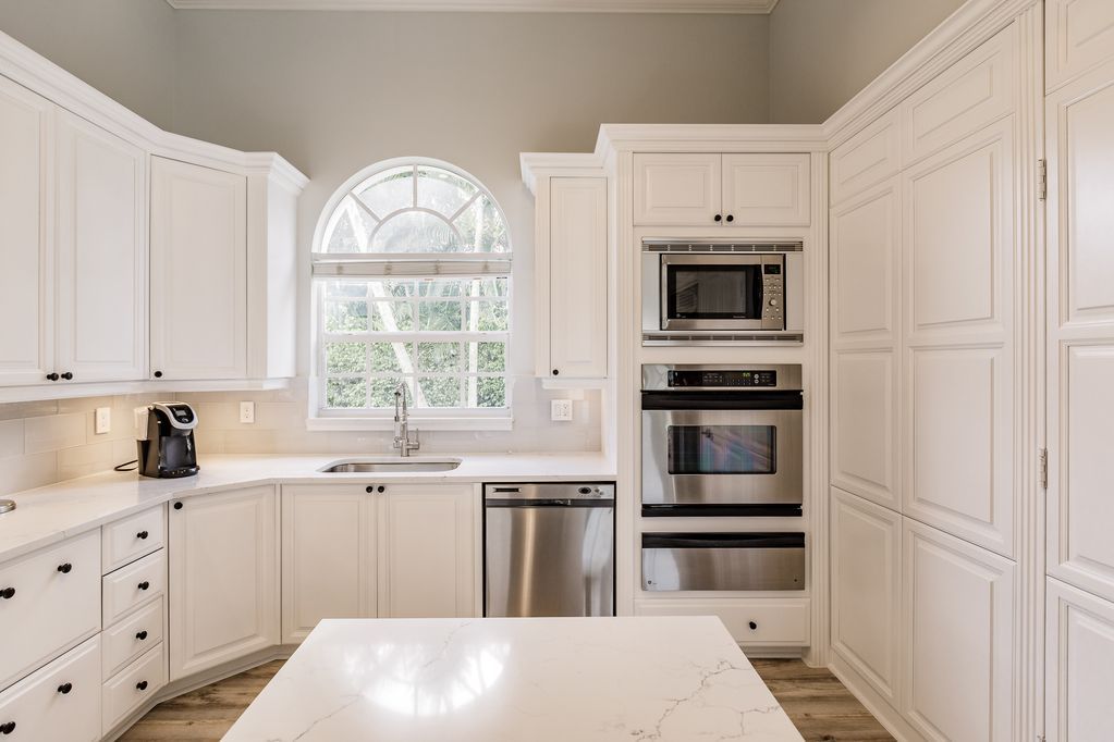 A kitchen with white cabinets , stainless steel appliances , and a large island.