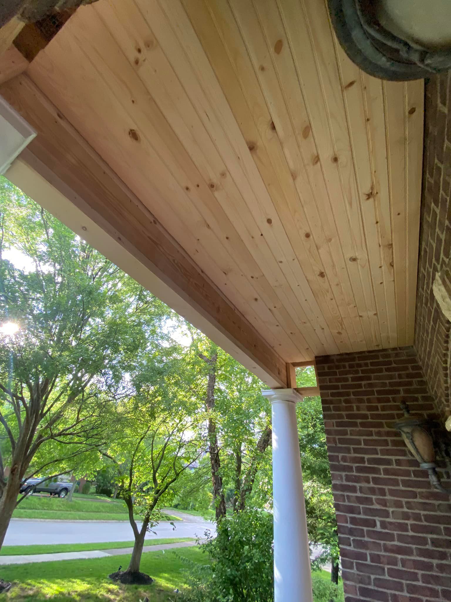 Wooden porch ceiling with exposed rafters, attached to brick and column.