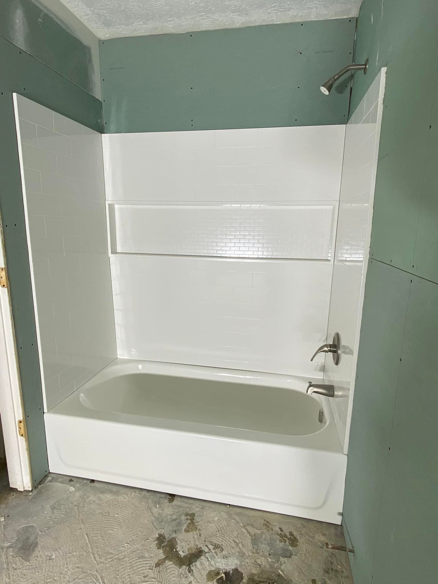White bathtub and shower surround installed in a bathroom under construction, with green drywall.