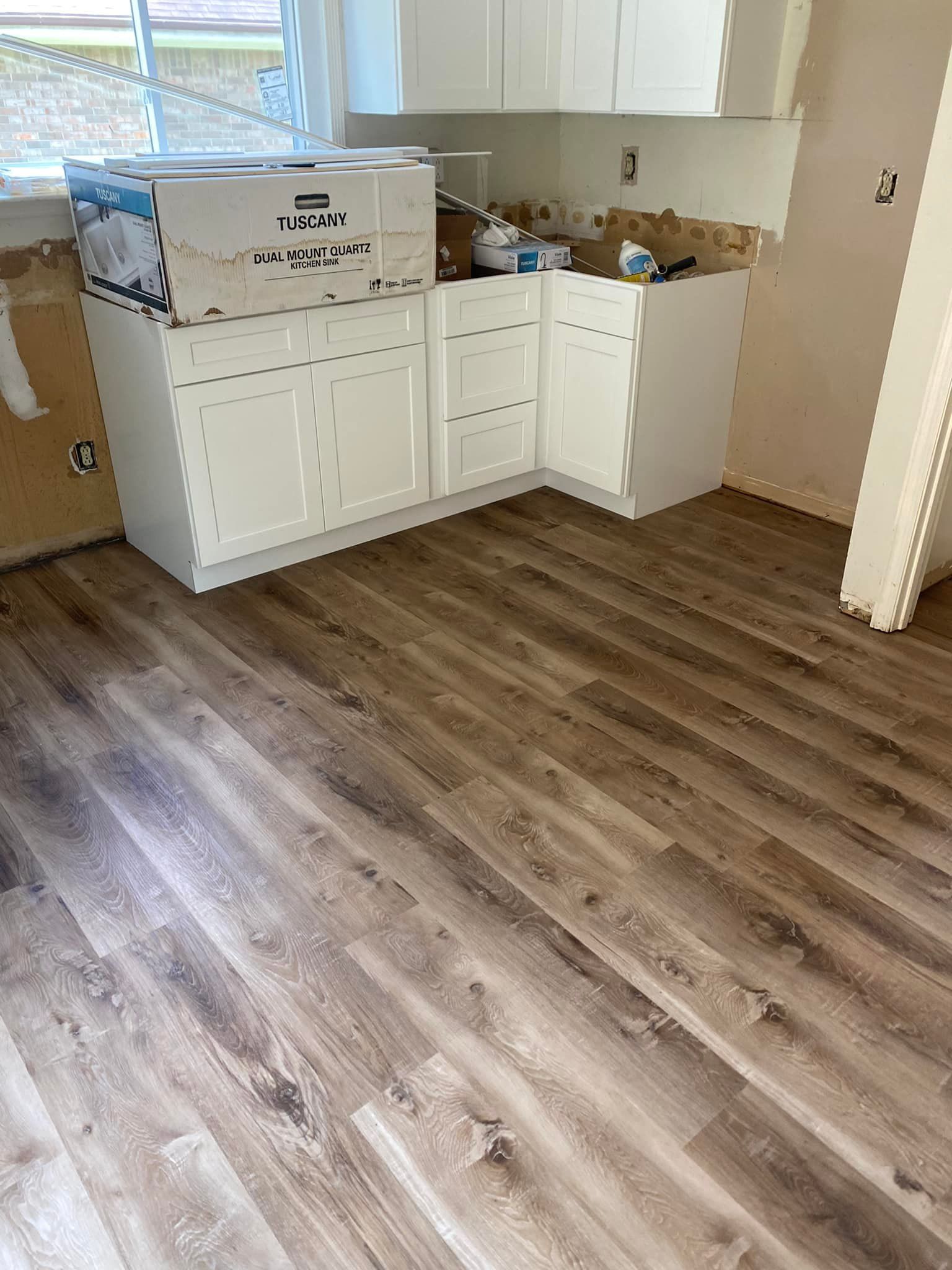 Kitchen with white cabinets, wood-look flooring, and boxes on the counter during renovation.