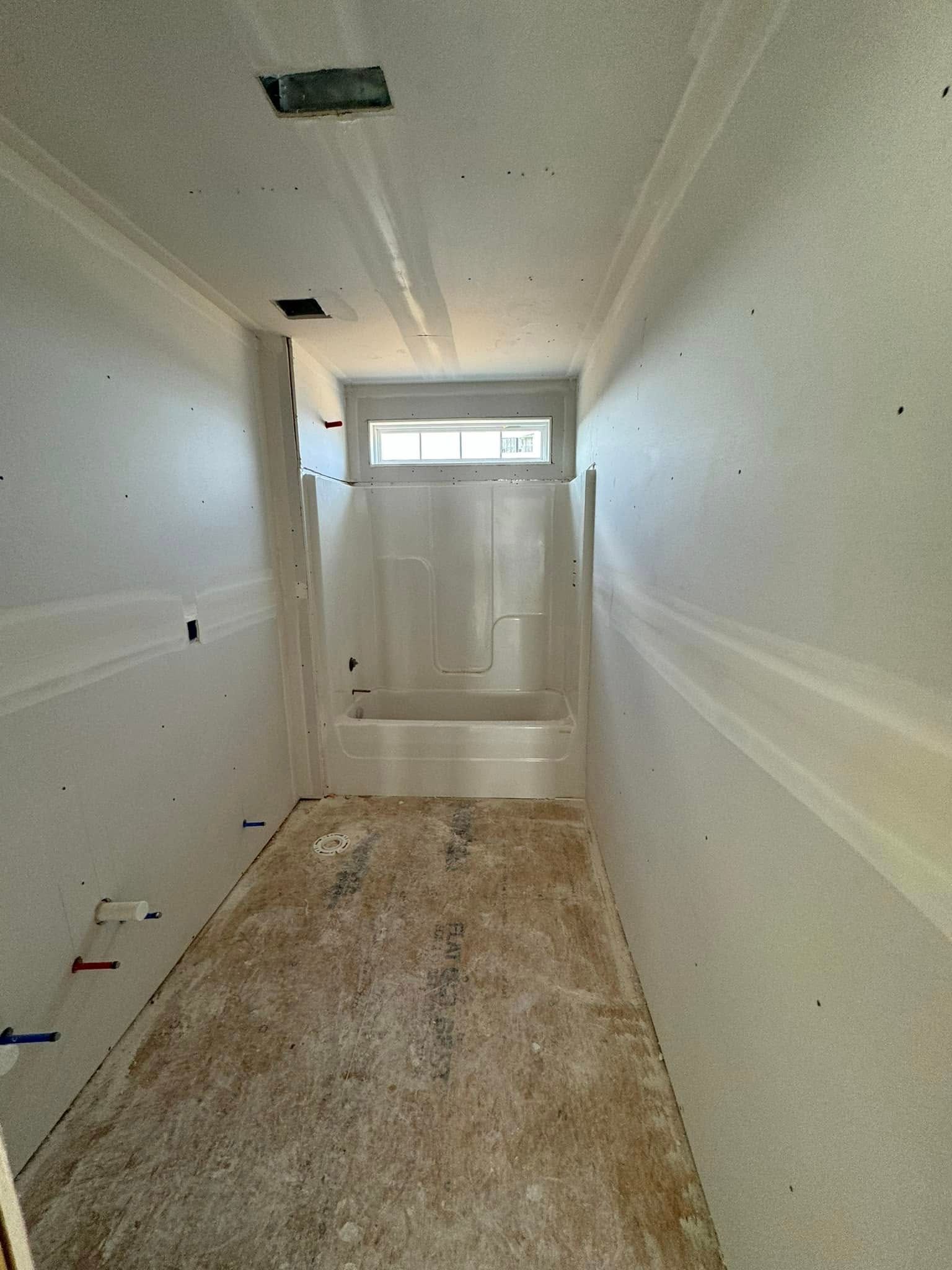 Unfinished bathroom with tub, window, drywall, and wooden subfloor.