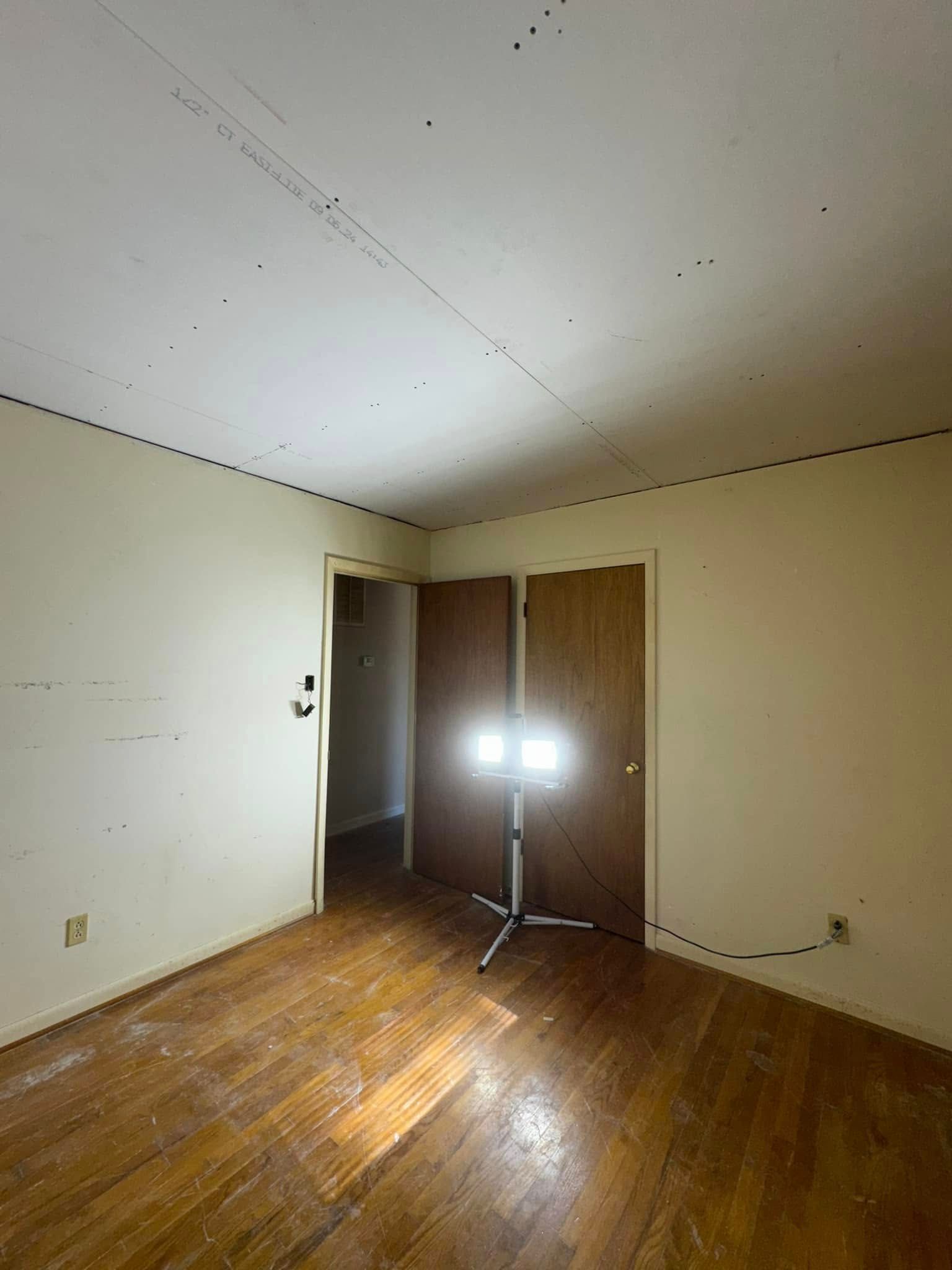 Empty room with worn wood floors, white walls, and a light on a tripod.