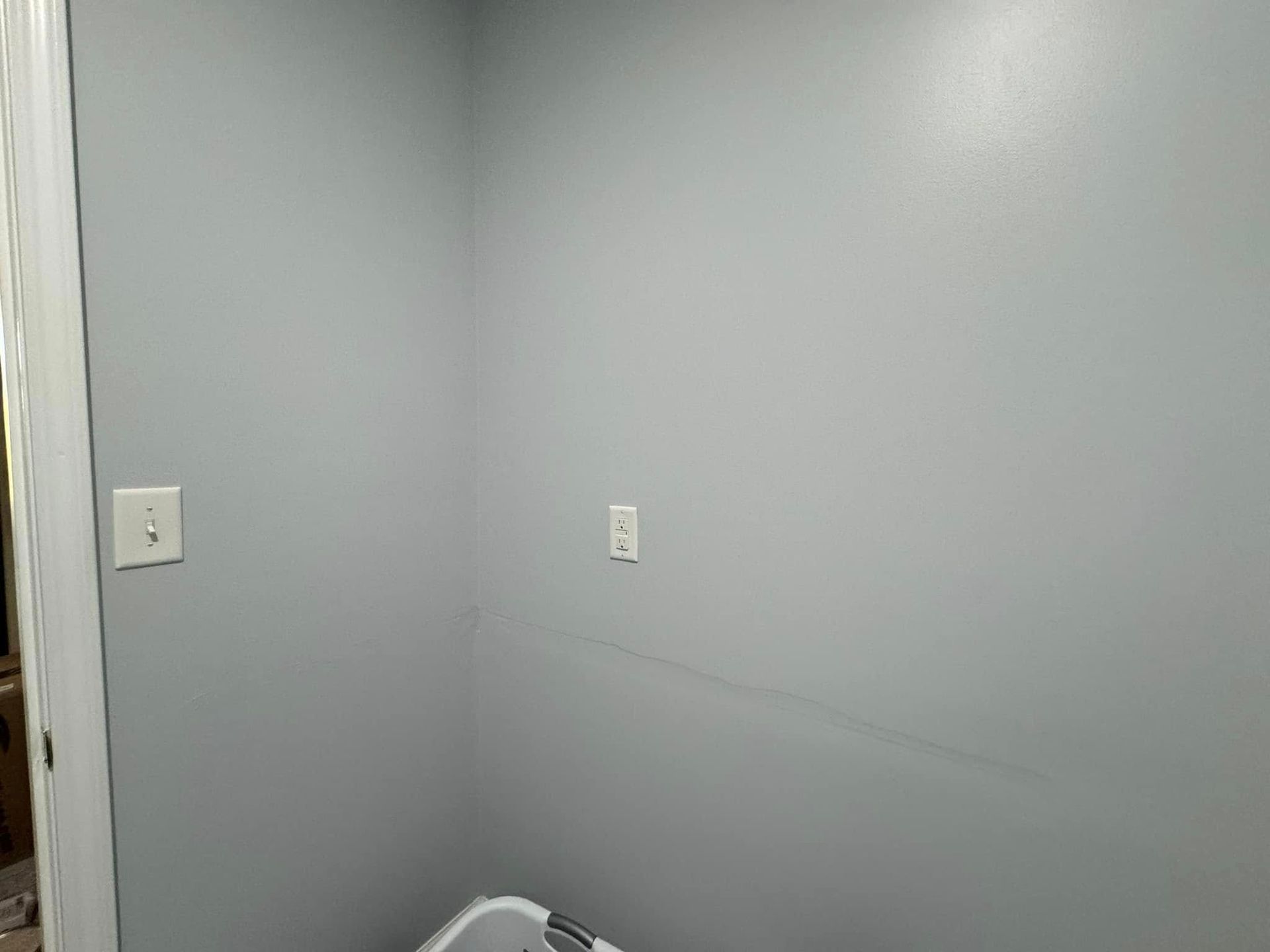 A gray-painted room corner with two outlets and a door on the left.