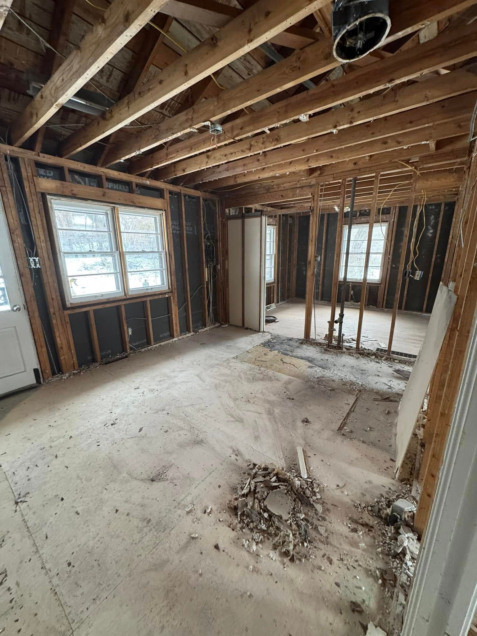 Interior of a room undergoing renovation; exposed beams, studs, and debris on the floor.