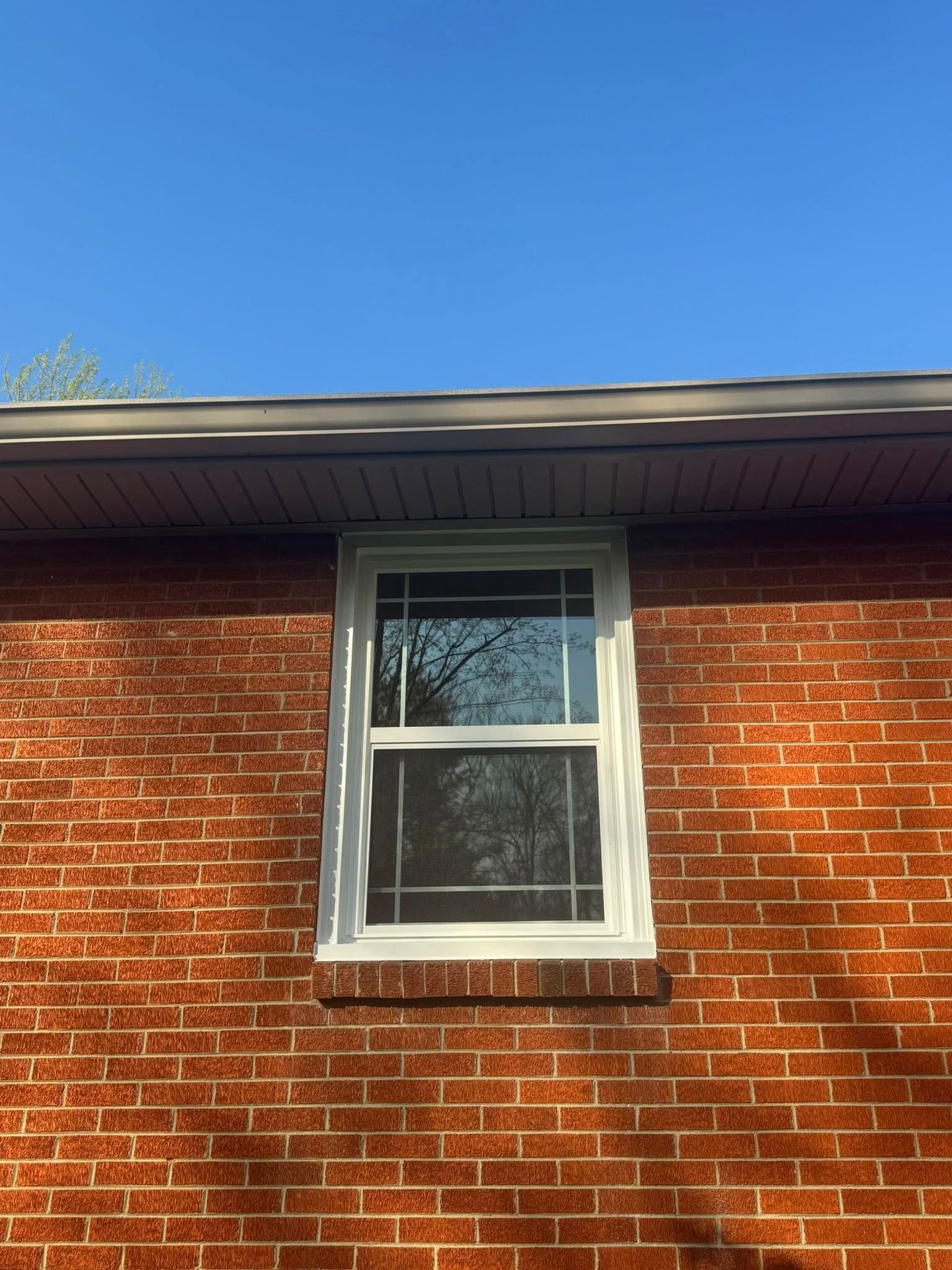 White-framed window on a red brick wall, beneath a dark roof and a clear blue sky.