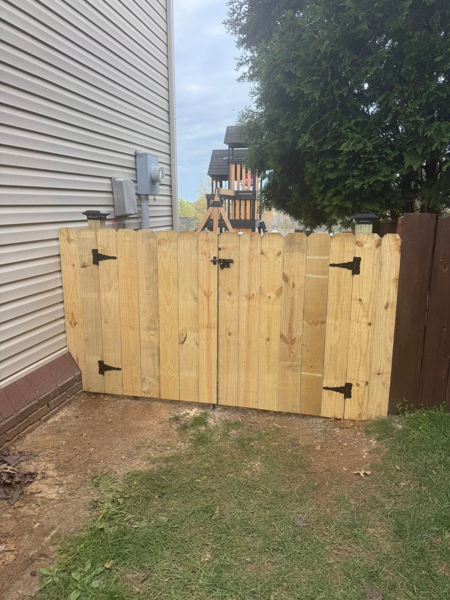 Wooden gate made of planks, attached to a house and a brown fence.