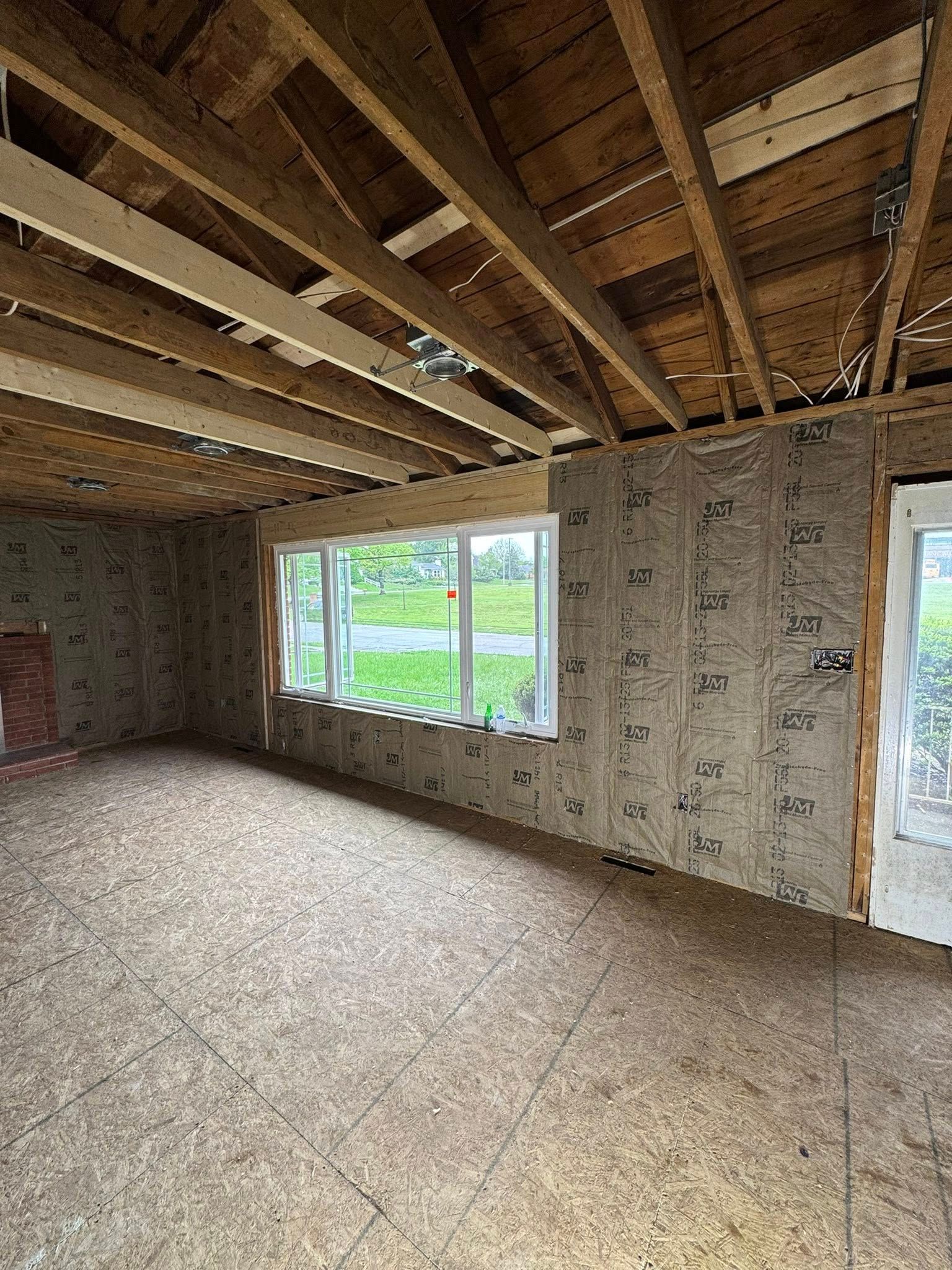 Interior of a room under construction, with exposed wooden beams, insulation on walls, and a window.
