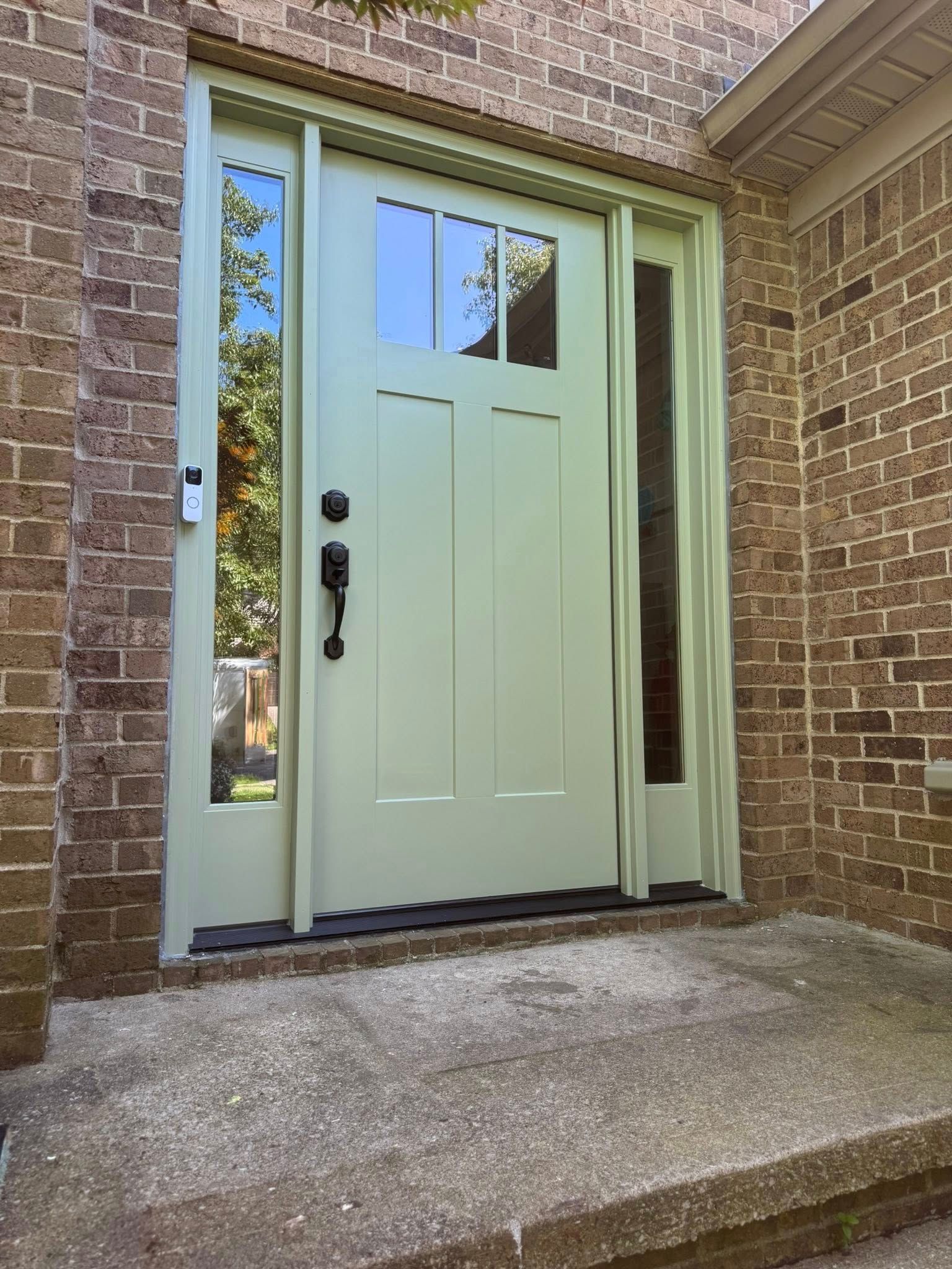 Light green front door with sidelights, set in a brick facade.