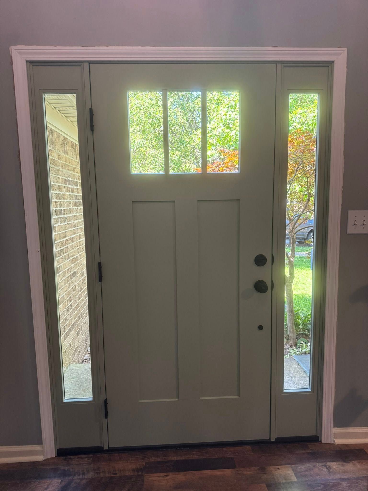 Green front door with glass panels and sidelights, white trim, brick wall visible.