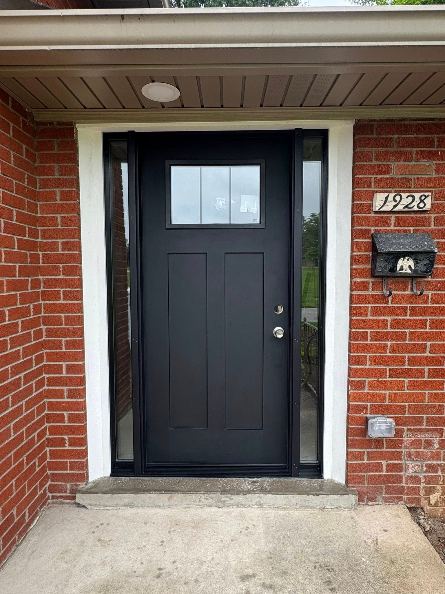 Black front door with sidelights, set in brick building. White trim and address plate.