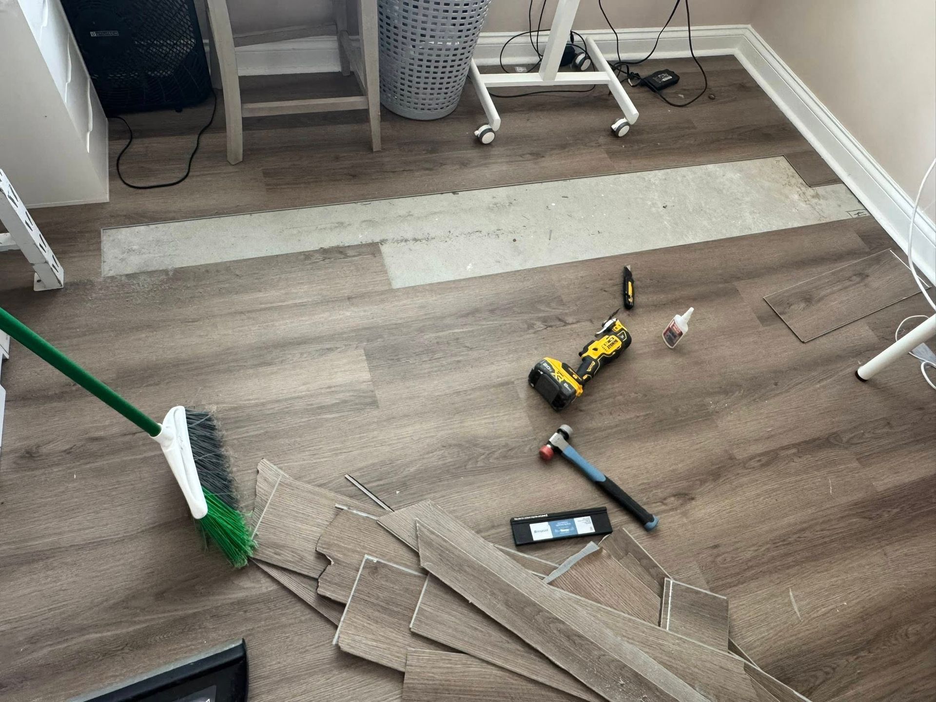 Room with flooring partially installed; tools, materials, and a broom are visible.