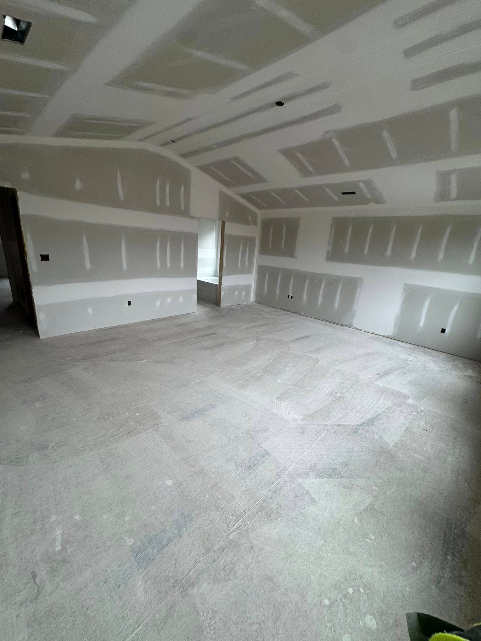 Interior of a room under construction, with drywall on walls and ceiling, bare concrete floor.