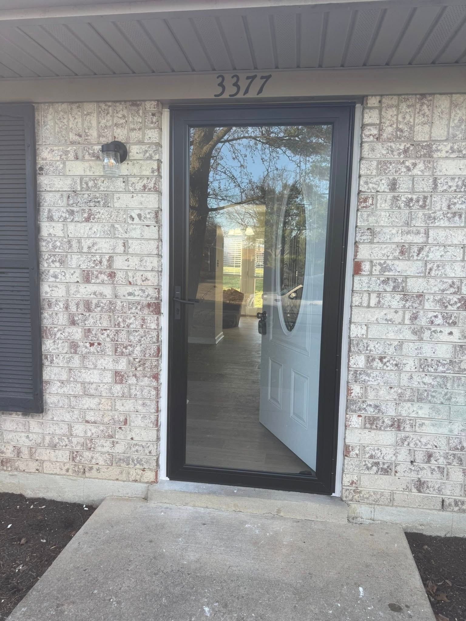 Front view of a house with an open glass storm door, white brick, and address number 3377 above the door.