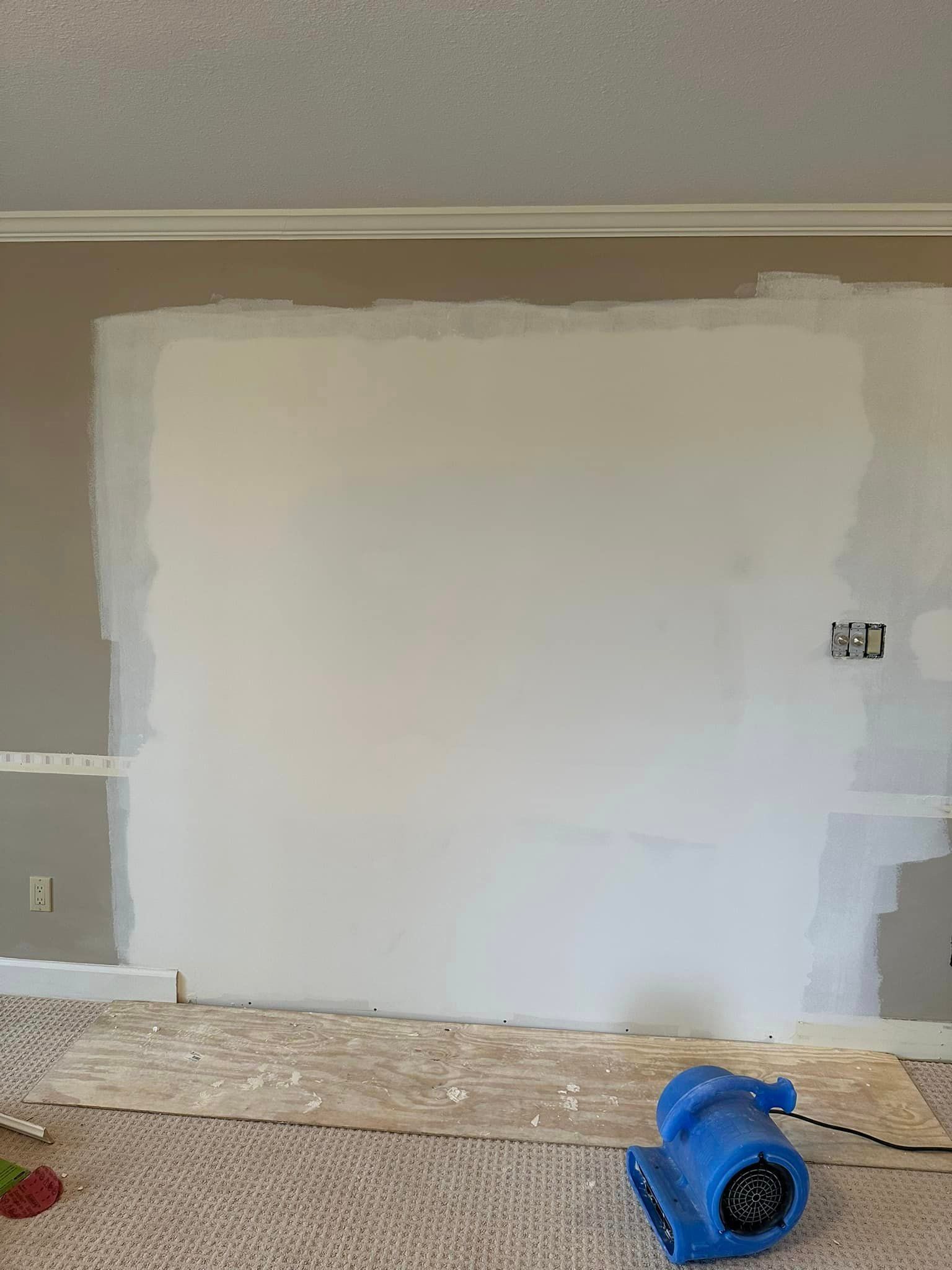 A room with a white wall and a blue air blower on the floor.