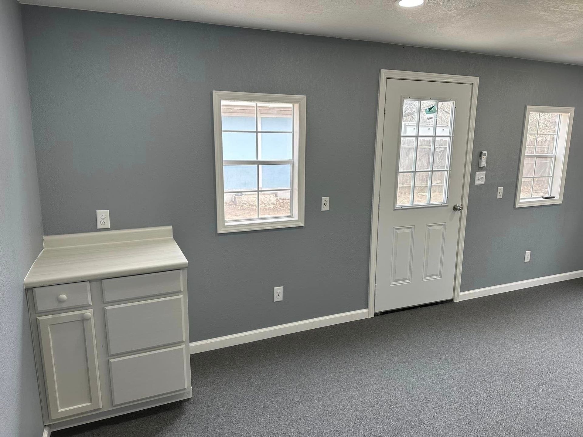 An empty room with a door and two windows.