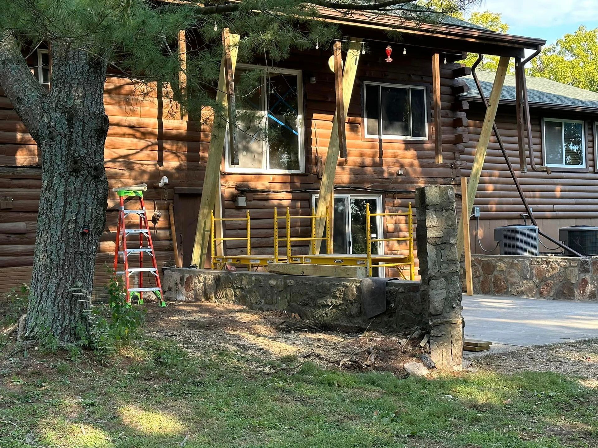 A log cabin with a porch and a ladder in front of it.
