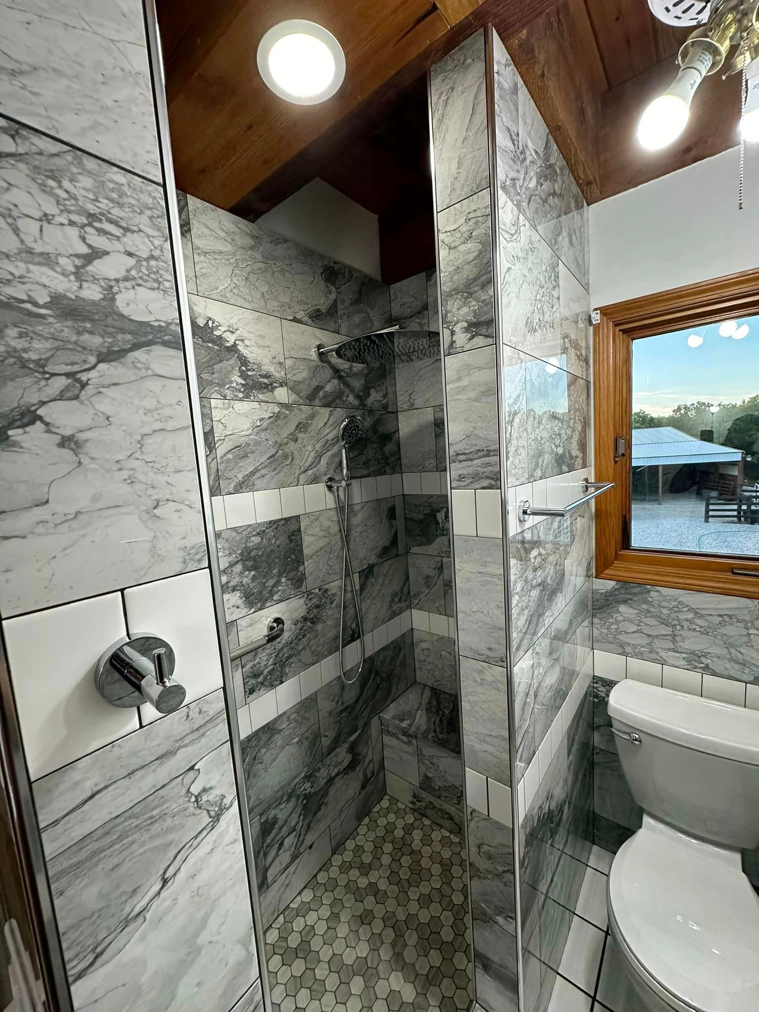 A bathroom with a walk in shower , toilet and window.