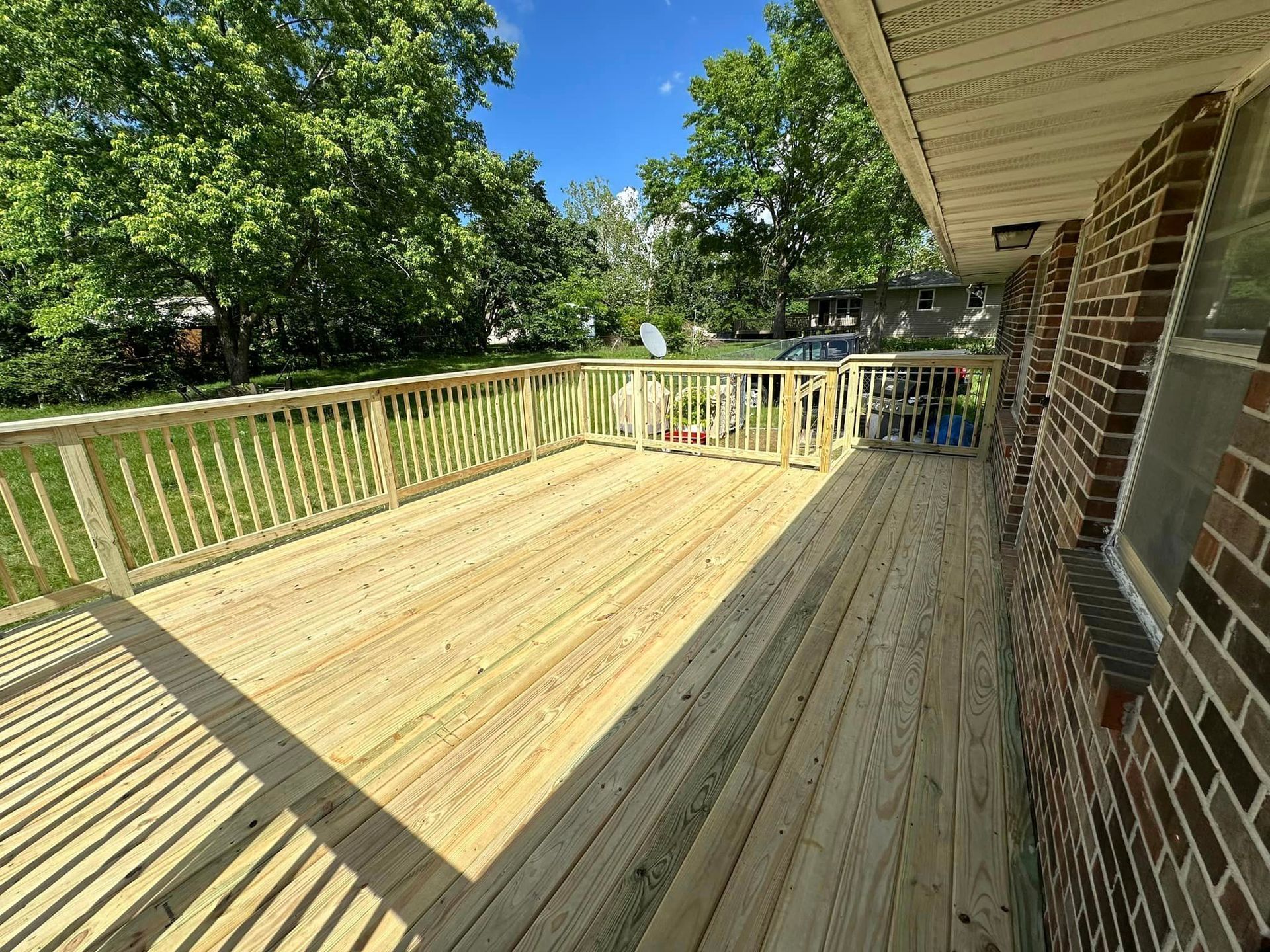 A large wooden deck with a railing on the side of a brick house.
