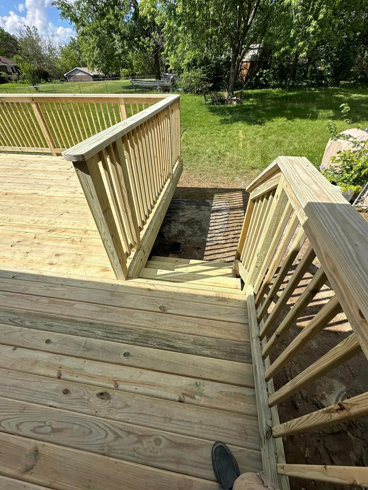 A person is standing on a wooden deck with stairs leading up to it.