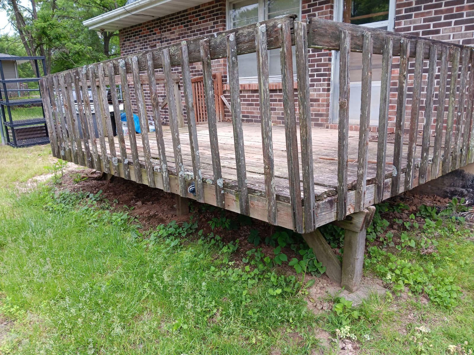 A wooden deck is sitting in the grass in front of a brick house.