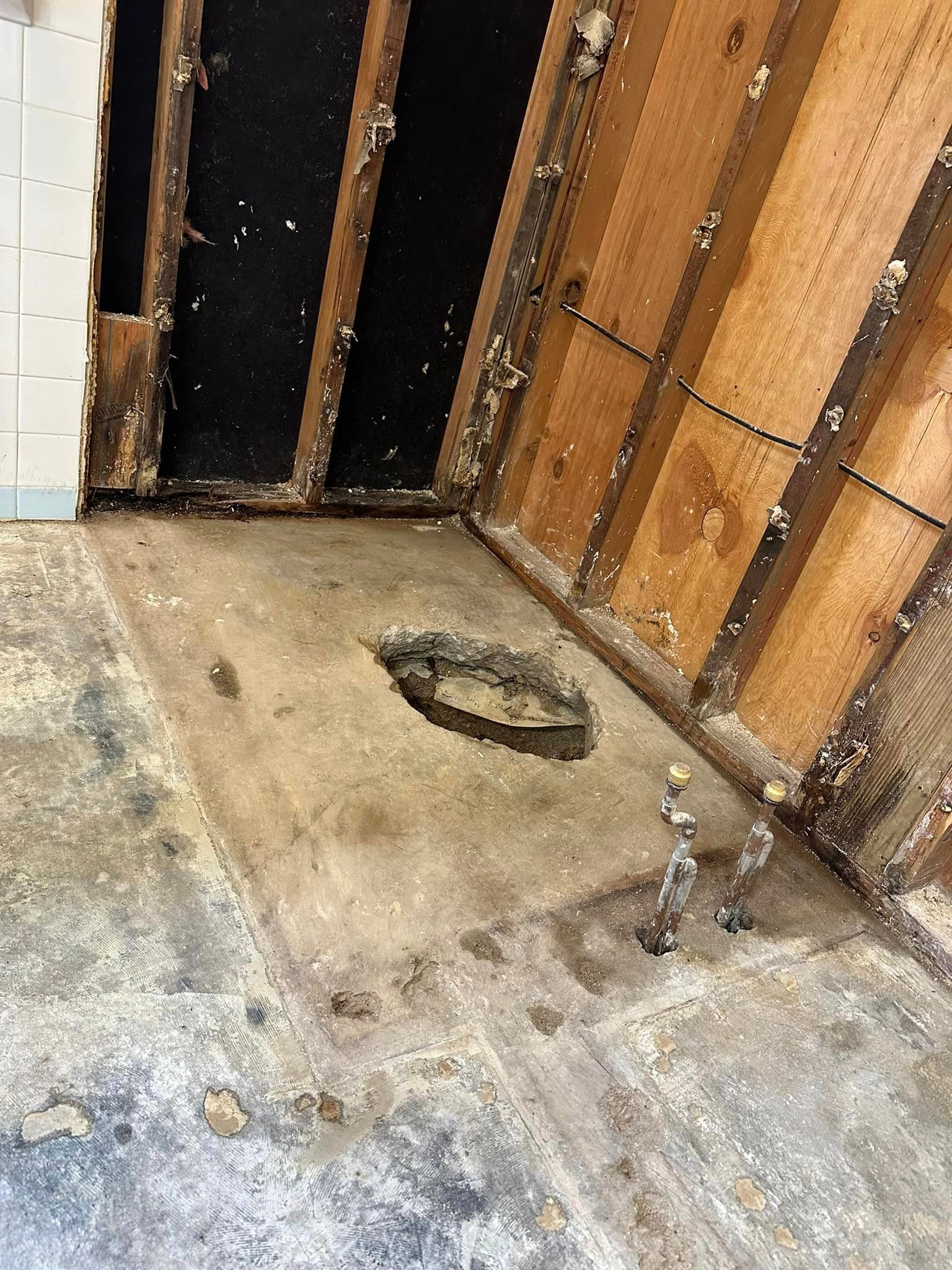 A bathroom with a hole in the floor and a wooden wall.