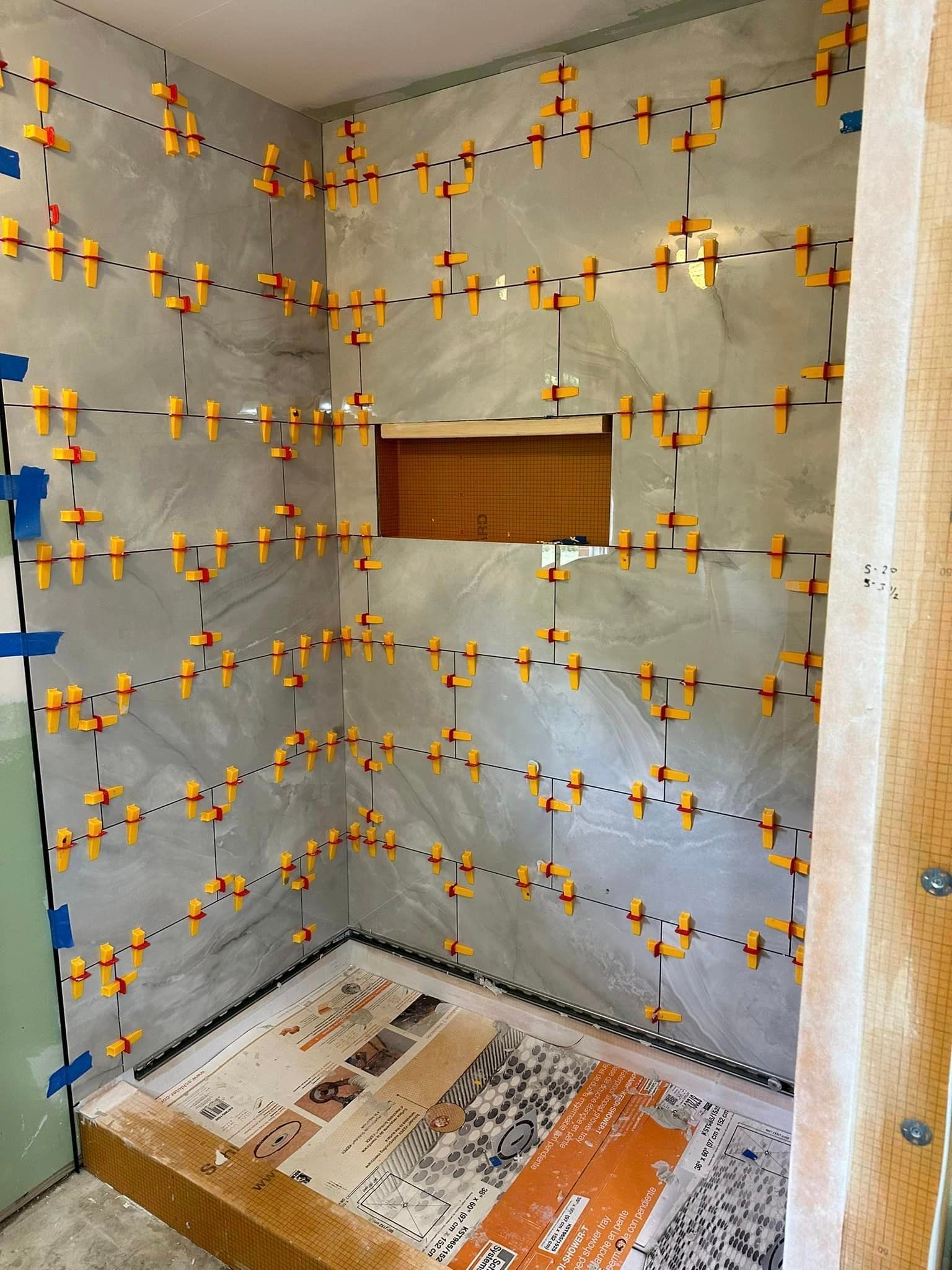 A bathroom with a shower stall being built and tiles being installed on the wall.