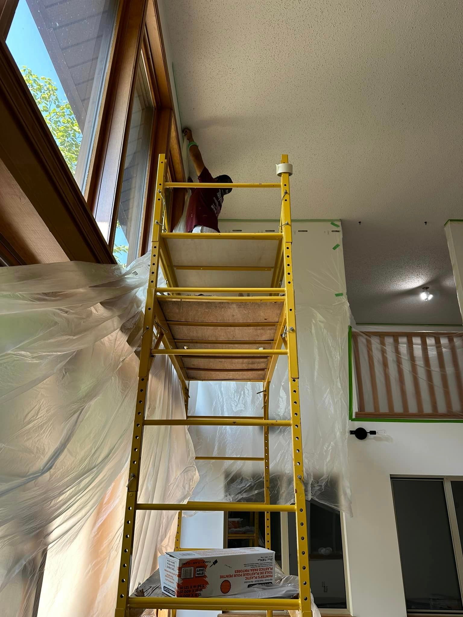 A person is standing on a yellow ladder in a room.