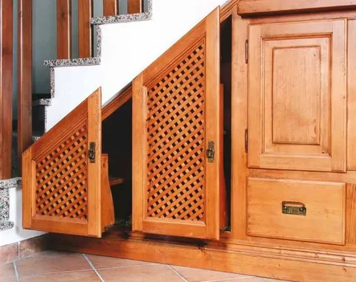 Un armadietto di legno sotto una rampa di scale con le ante aperte