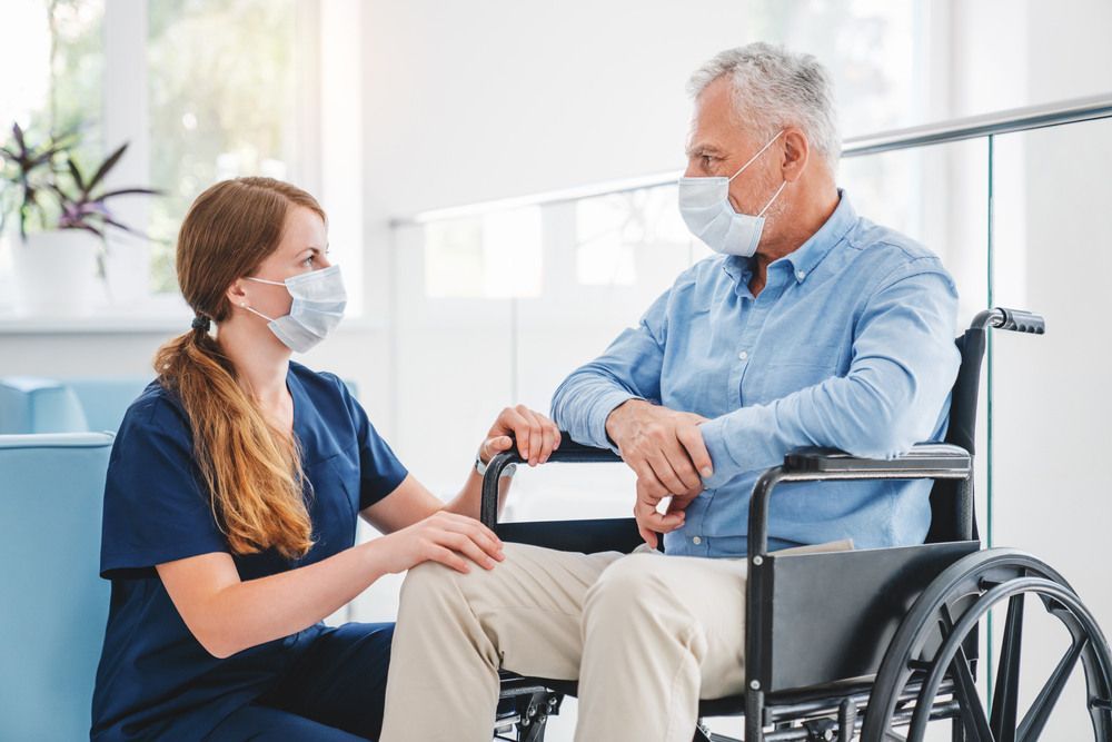 Nurse Wearing a Mask is Talking to an Elderly Man in a Wheelchair — Universal Nurse in Yarraman, QLD