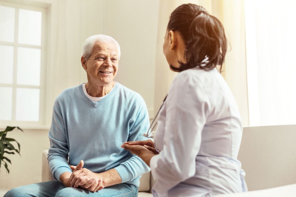 An Elderly Man is Sitting on a Couch Talking to a Doctor — Universal Nurse in Blackbutt North, QLD