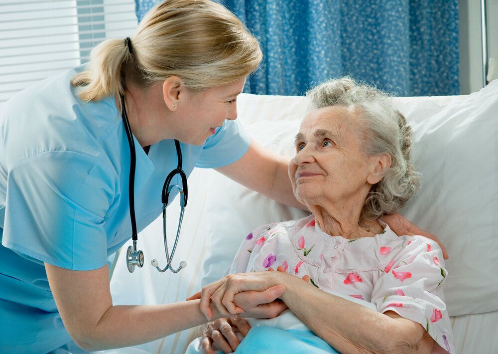Nurse is Holding the Hand of an Elderly Woman in a Hospital Bed — Universal Nurse in Blackbutt North, QLD
