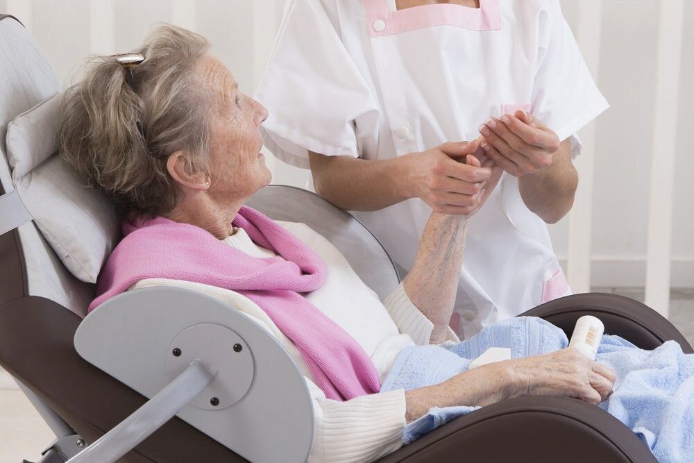 A Nurse Is Holding The Hand Of An Elderly Woman In A Hospital Chair — Universal Nurse in Blackbutt North, QLD