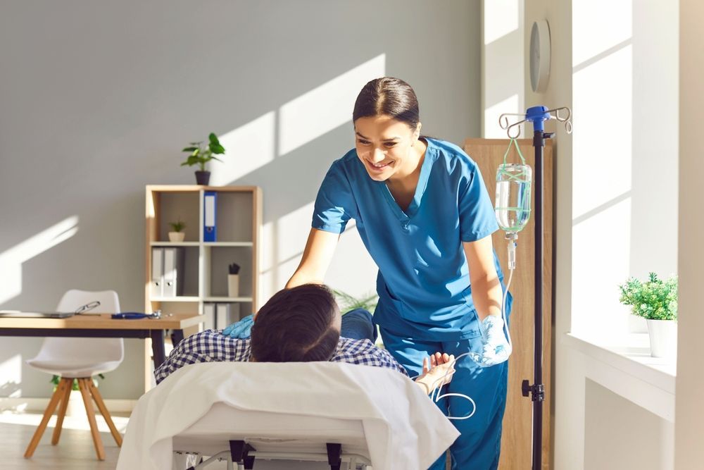 Nurse in Blue Scrubs Smiles at Patient Receiving IV Fluids — Universal Nurse in Blackbutt North, QLD