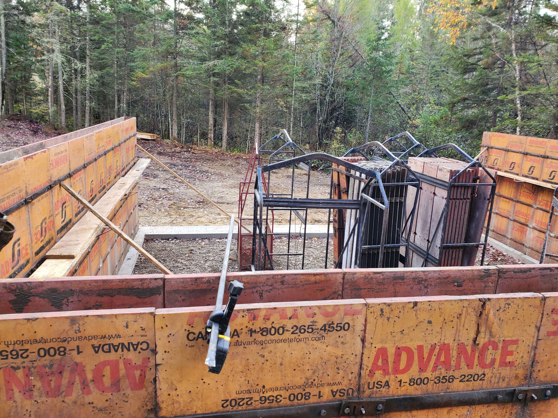 Chantier : Des coffrages orange maintiennent une armature en béton pour une structure en béton, installée dans une clairière avec des arbres en arrière-plan.