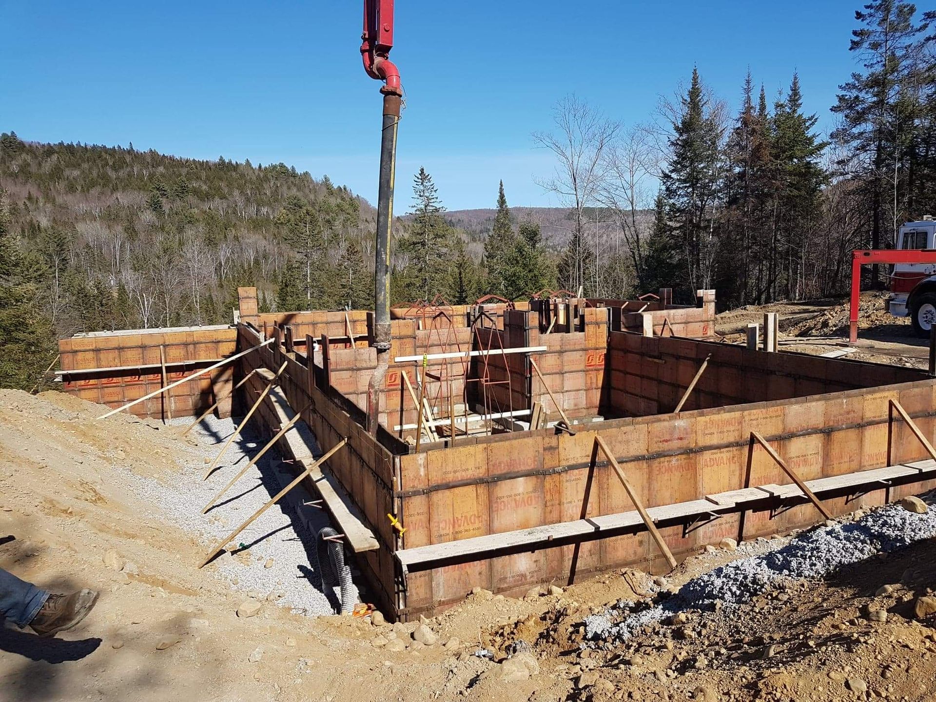 Du béton est coulé dans des coffrages en bois pour les fondations d'un bâtiment dans une zone boisée.