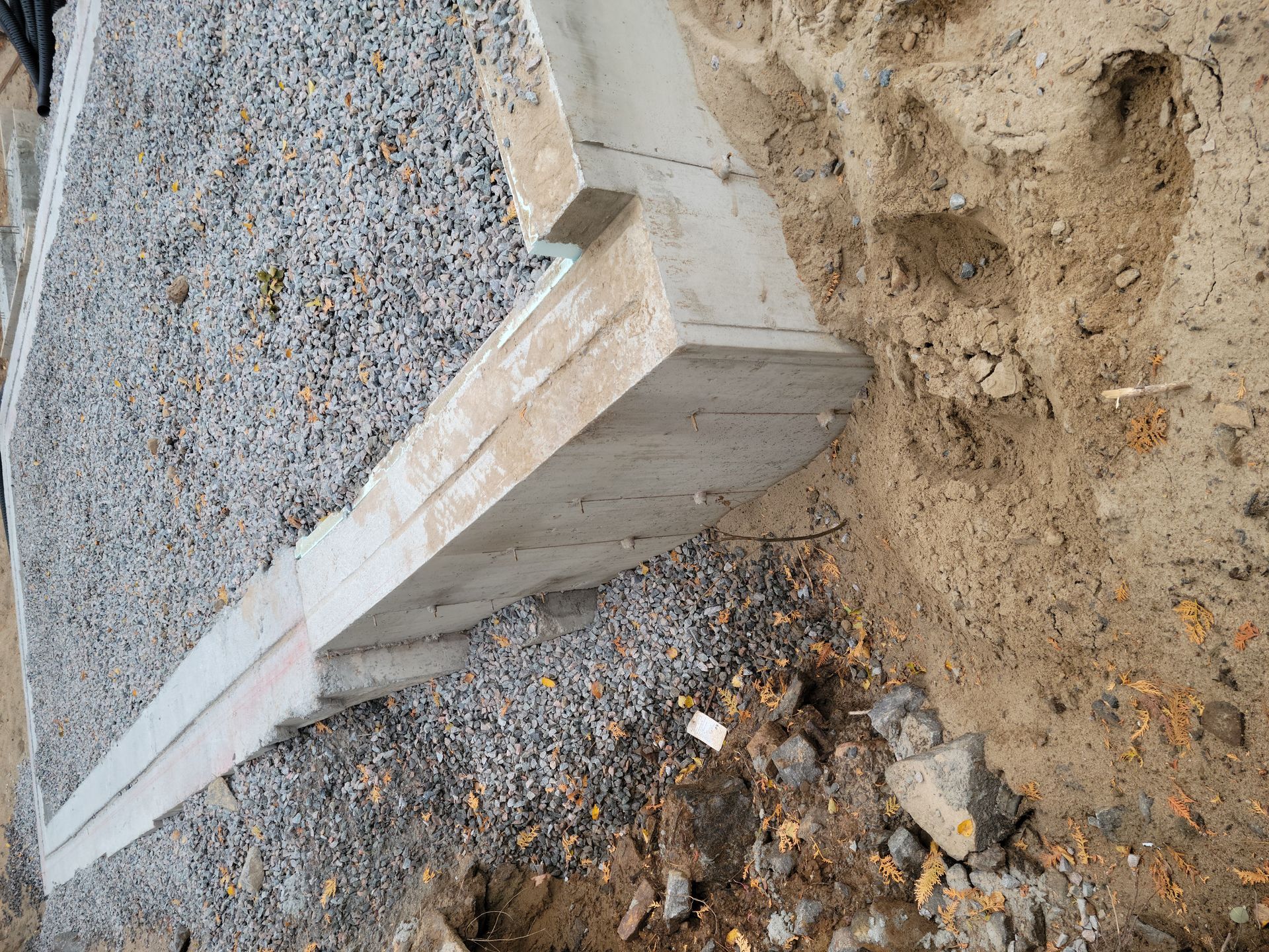 Mur de fondation en béton avec du gravier d'un côté et de la terre de l'autre.