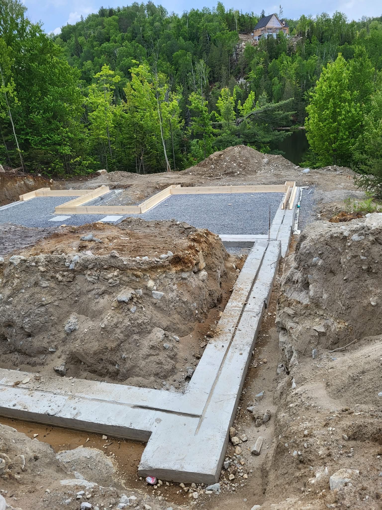 Chantier de construction de fondations avec semelles en béton et base en gravier dans un environnement boisé.