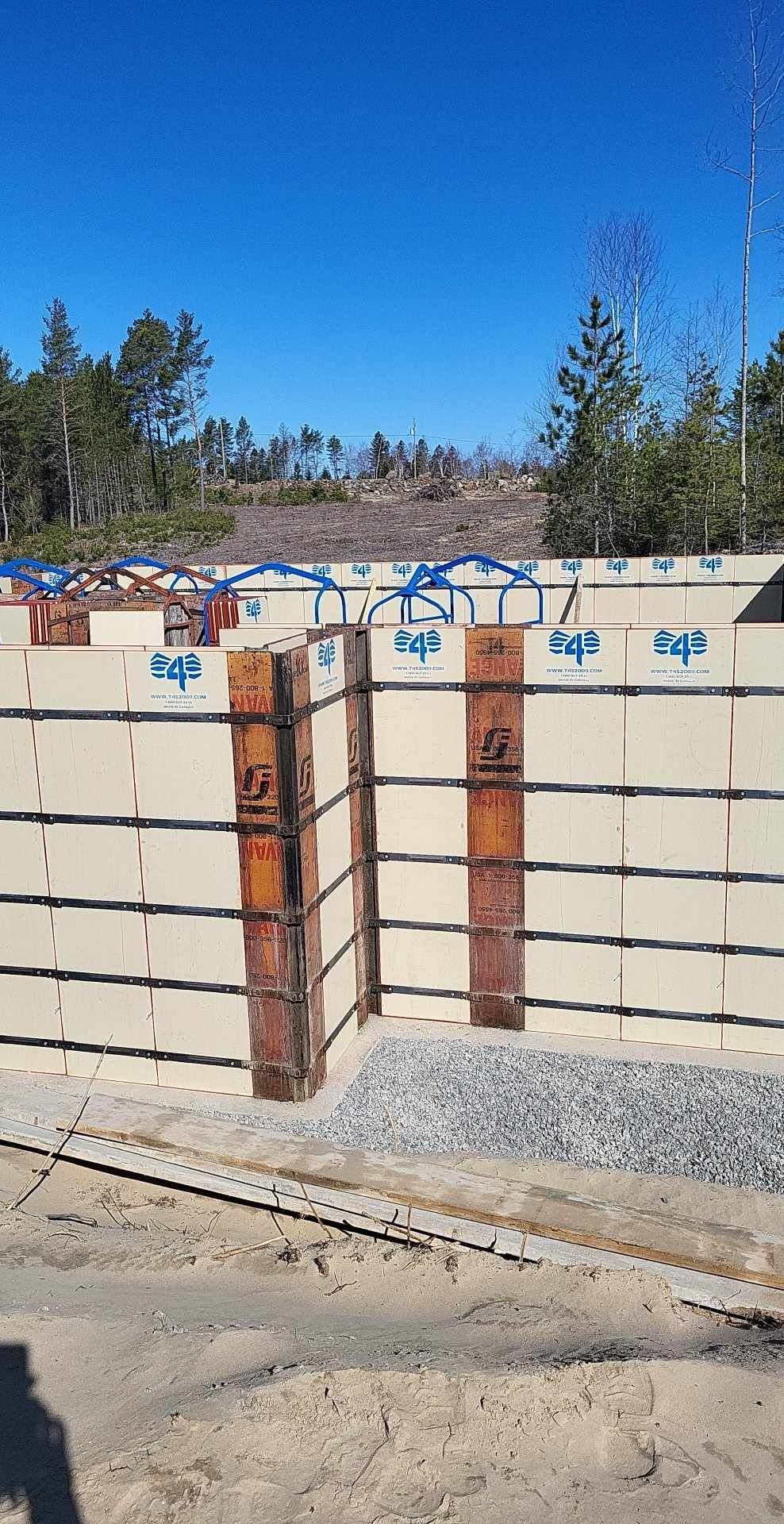 Des blocs de béton formant un mur de soutènement, soutenus par des équerres métalliques, sous un ciel bleu.