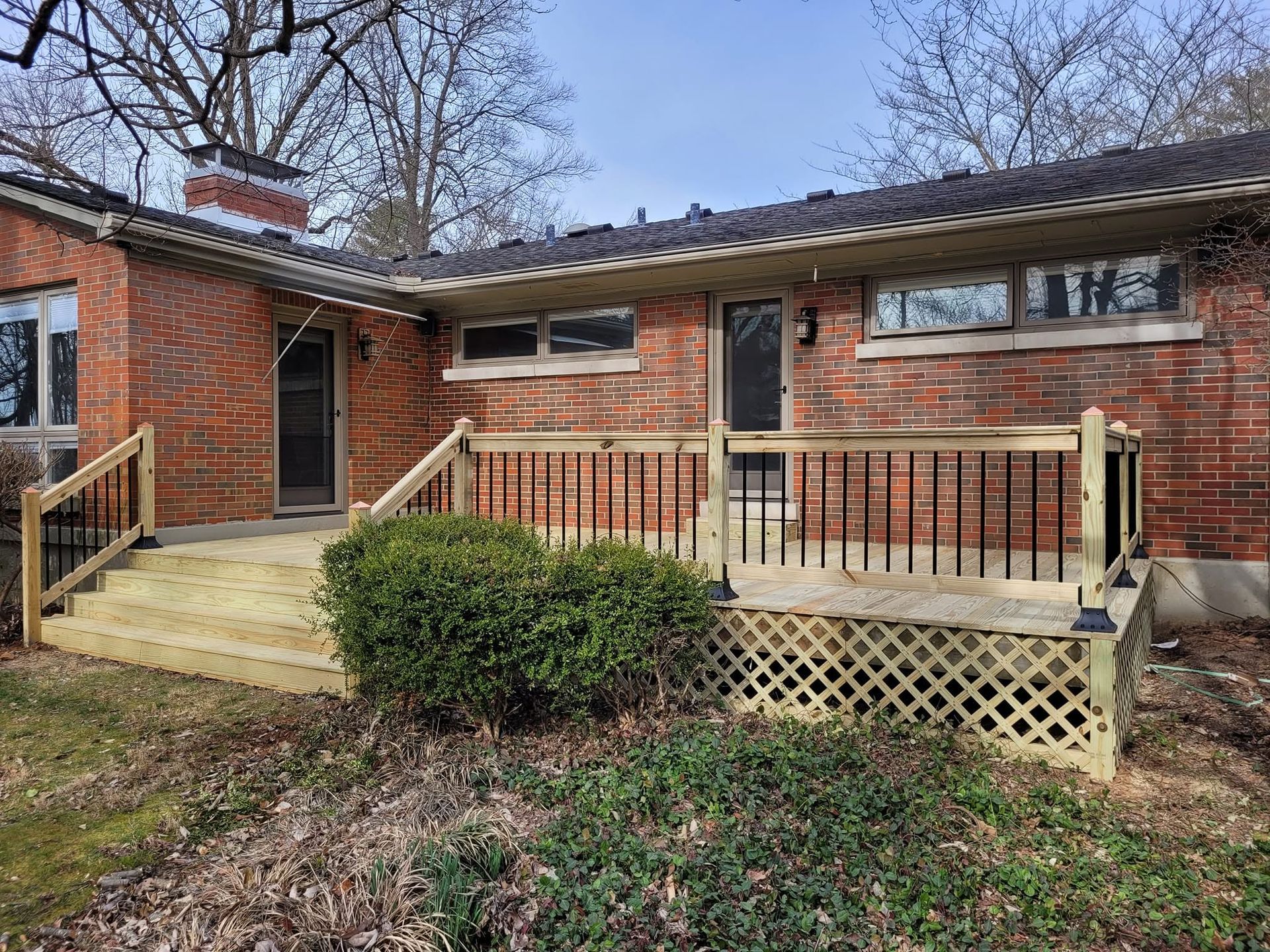 Brick house exterior with a wooden ramp, porch railing, and shrubbery in front