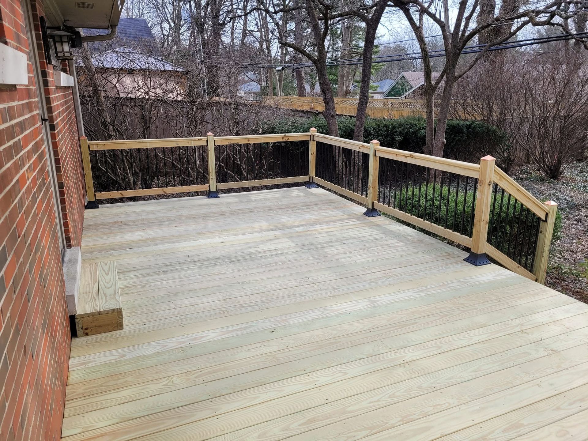 Wooden deck overlooking a yard with bare trees and a brick house wall