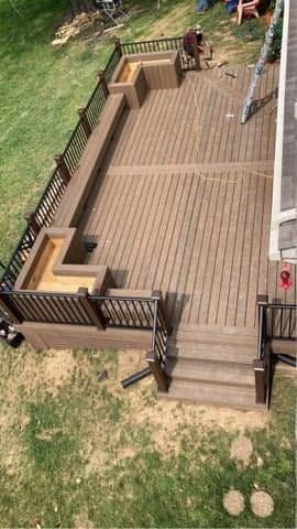 Wooden backyard deck with railings, steps, and seating area, seen from above.