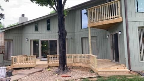 Two-story gray house with wooden decks and a large tree in the front yard