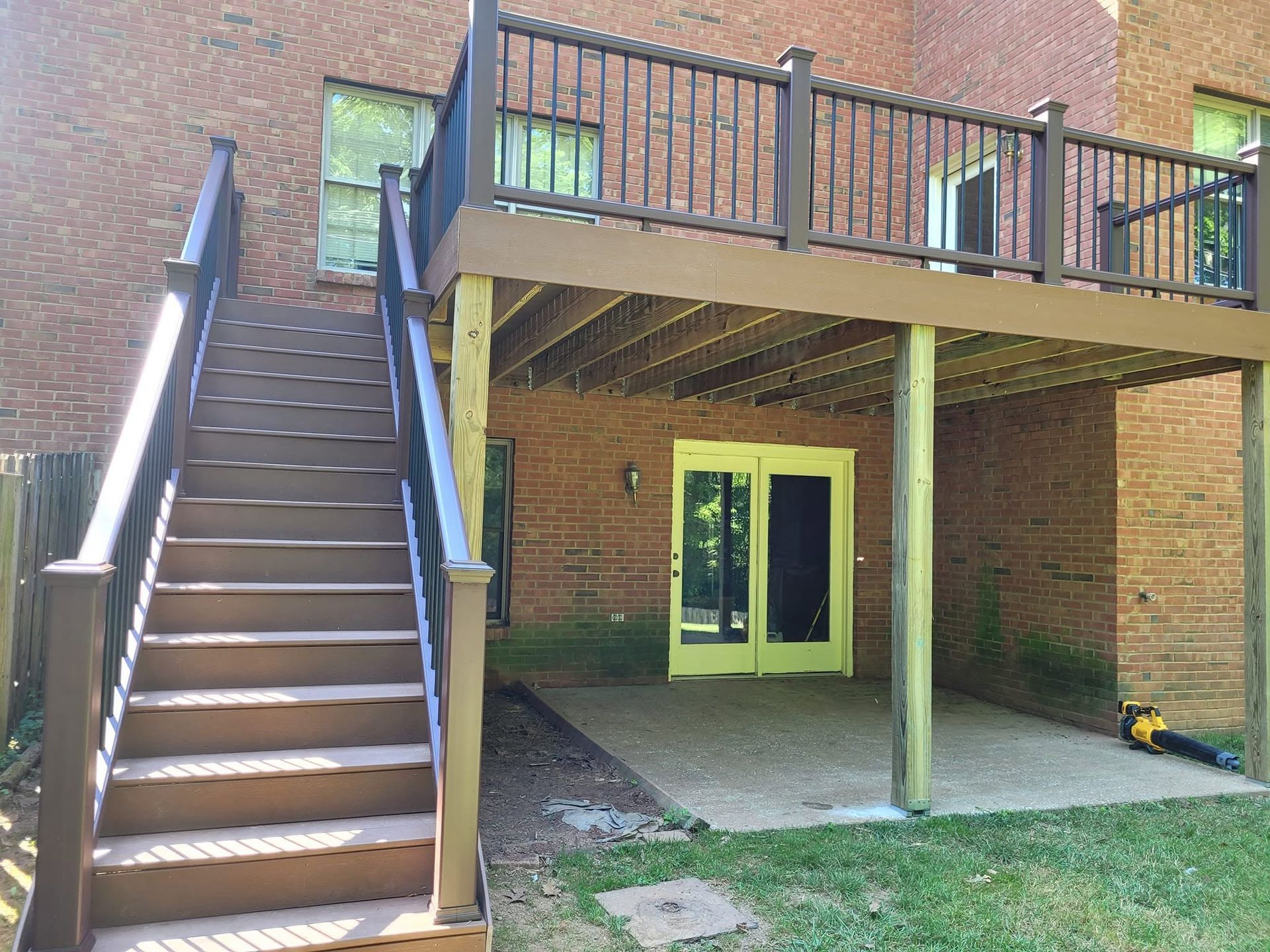 Brick apartment patio with exterior stairs, upper deck, and double glass doors under the deck