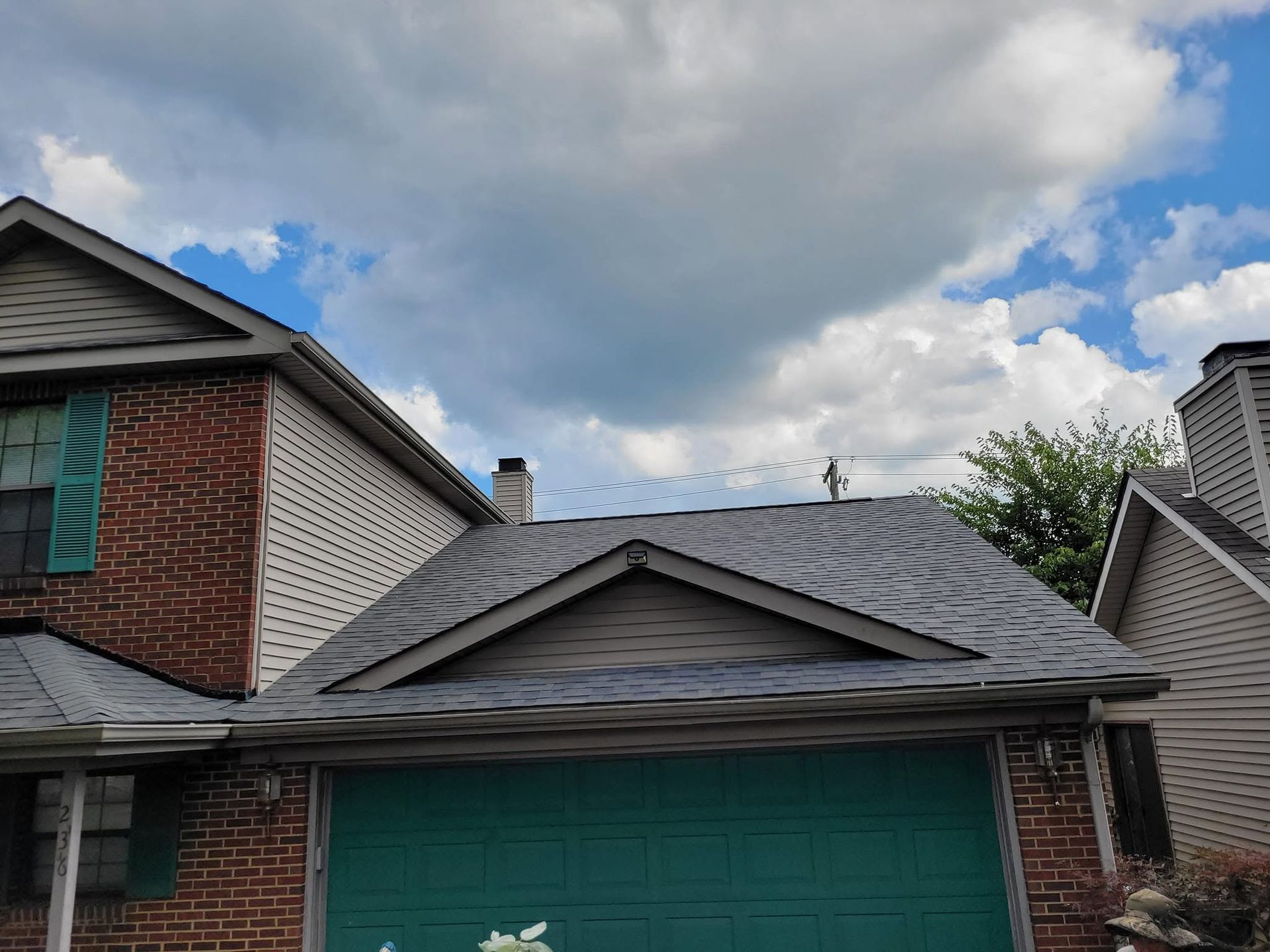 Suburban house with green garage door, gray roof, red brick and white siding under cloudy sky
