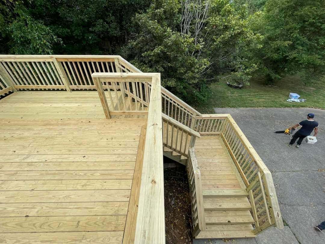 Wooden deck and stairs overlooking a gravel path, with a person sitting on a chair below